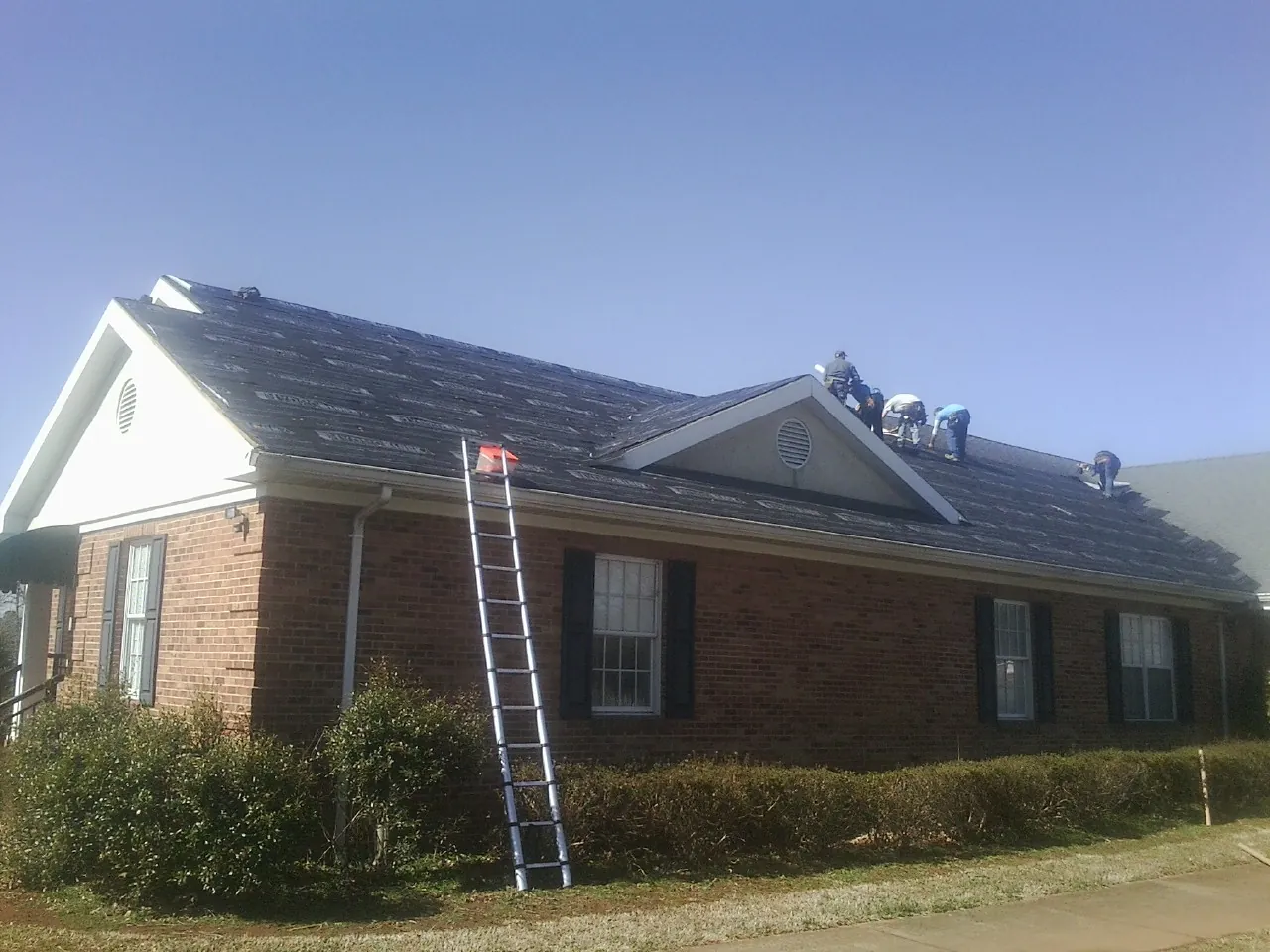 Crew tearing shingles off a brick ranch roof with a ladder set — Metal Roof Repair work by our crew in Mount Vision