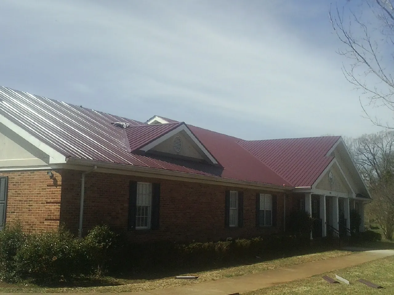 Red metal roof with gabled entries on a long brick building, from a Hail Damage Roof Repair job in Mount Vision