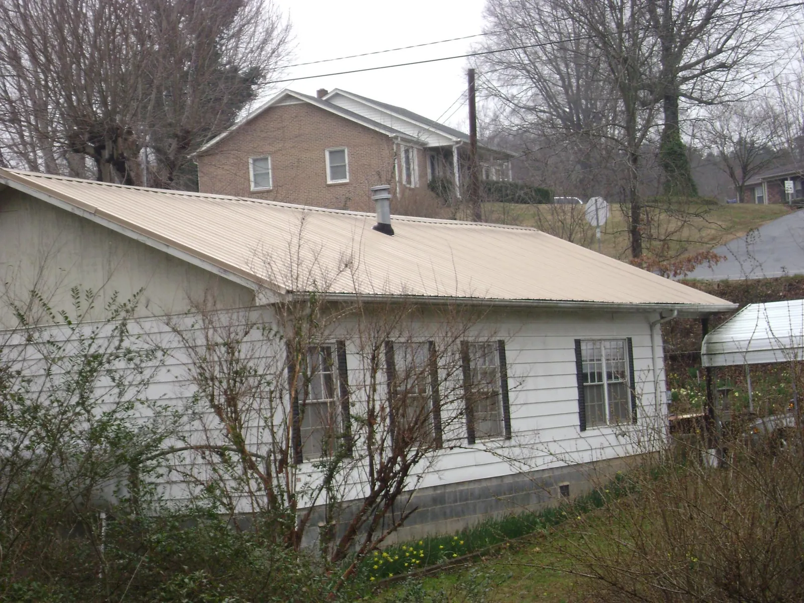 Tan metal roof on a white sided house set into a hillside — Commercial Roofing by Roofing Brothers in Mount Vision