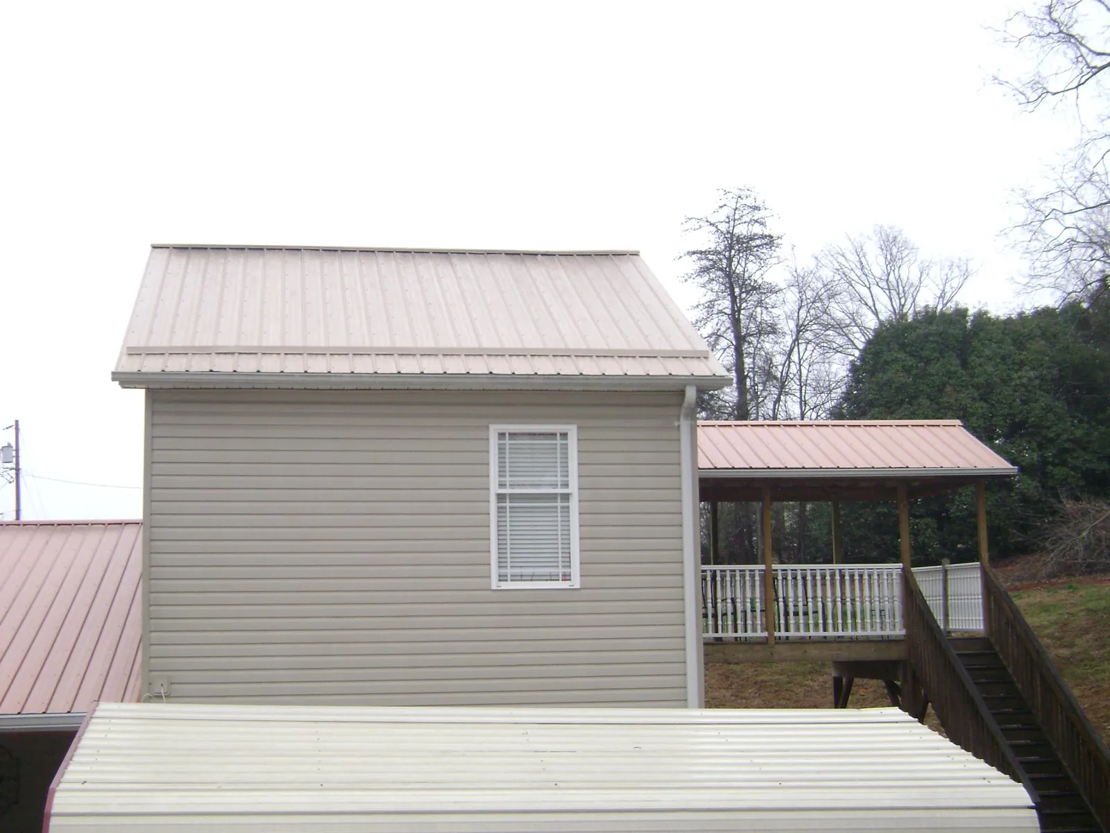 Tan metal roofs on a two story addition and attached porch, from a Roof Replacement job in Mount Vision